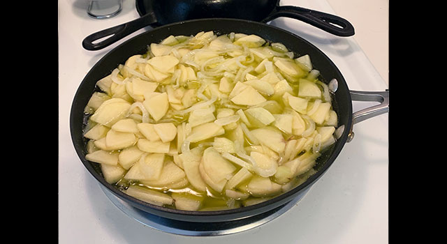 Sliced potatoes and onions simmering in a skillet on a stovetop